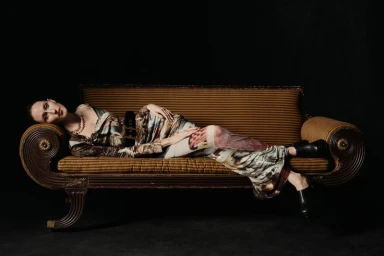 Model lying horizontally on a striped vintage settee wearing a patterned garment for Vivienne Westwood fall/winter 2024 lookbook