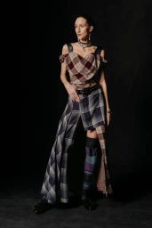 Anna Cleveland wearing an asymmetrical plaid corset top and draped tartan skirt against a black backdrop for Vivienne Westwood.