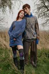 Two models standing outdoors in a field wearing patterned knitwear and knee-high socks for Vivienne Westwood