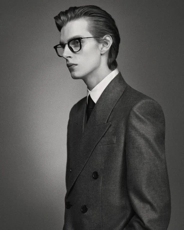 Monochromatic portrait of a blond male model wearing glasses and a double-breasted suit in a studio. Fashion portrait in black and white.