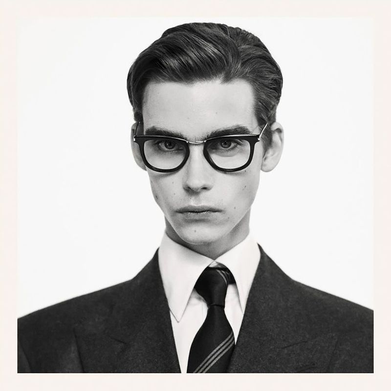 Portrait of a young adult male with dark hair and glasses wearing a suit and tie against a neutral, light background in a studio shot.