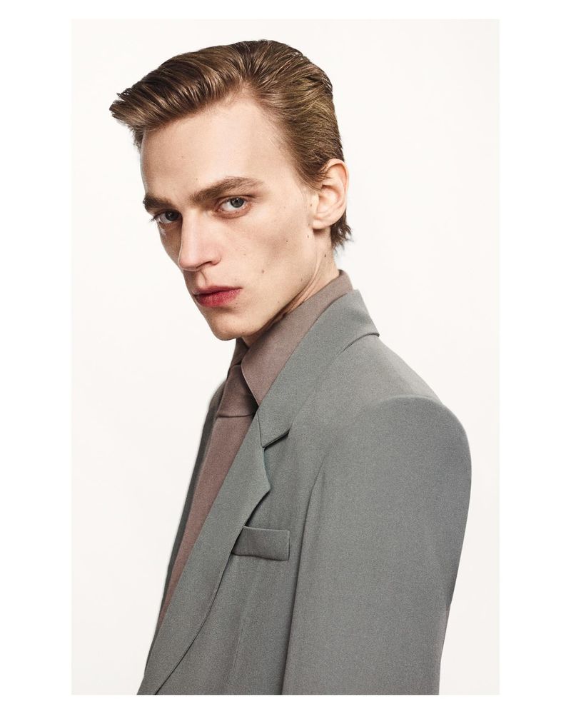 Portrait of an adult male in a gray suit and brown shirt against a white background. Fashion shot with simple wardrobe and lighting.