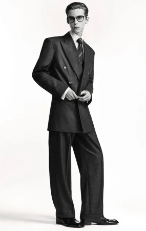 Male model wearing black eyeglasses and a charcoal double-breasted suit against a pure white studio backdrop.