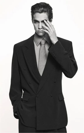 Monochrome portrait of a man in a suit with his hand near his face, posing in a photo studio against a white backdrop.