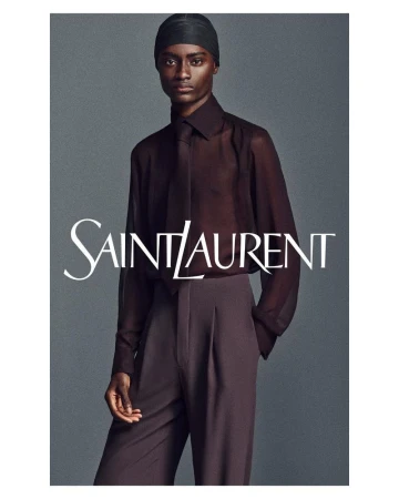 Dark-skinned adult fashion model poses in a sheer dark top and high-waisted trousers for a studio fashion shot, promoting Saint Laurent.