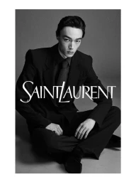 Monochrome portrait of a seated man wearing a black suit and tie against a plain grey background with Saint Laurent text overlay.