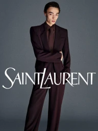 Man wearing a dark brown suit and tie against a plain grey backdrop with white Saint Laurent logo overlay