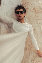 Man wearing sunglasses and white long-sleeve shirt relaxing in a hammock on a sandy beach for Zara Man S/S 24