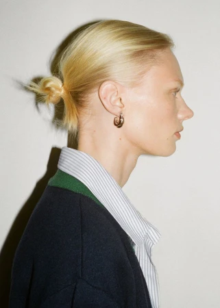 Profile portrait of a blonde woman wearing a striped shirt and dark cardigan against a white background