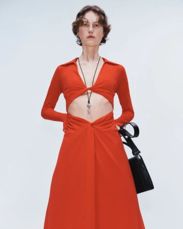 Julie Hoomans wears a long-sleeved red cutout dress and holds a black handbag against a seamless light studio background.