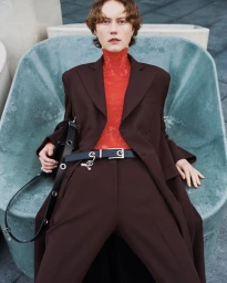 Model wearing a dark brown suit jacket and trousers with an orange patterned top seated in a large turquoise basin