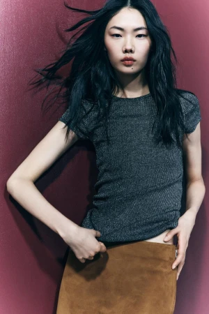 Fashion shot of an Asian woman with long black hair in a gray ribbed top and brown skirt against a maroon background in portrait orientation.
