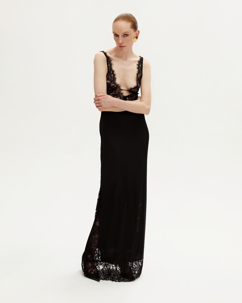 Elegant woman in a black lace dress poses against a white background, showcasing fashion and style in a studio setting.