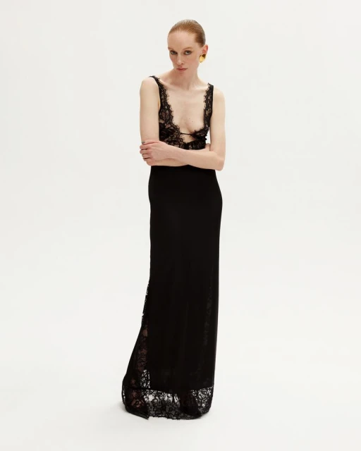 Elegant woman in a black lace dress poses against a white background, showcasing fashion and style in a studio setting.