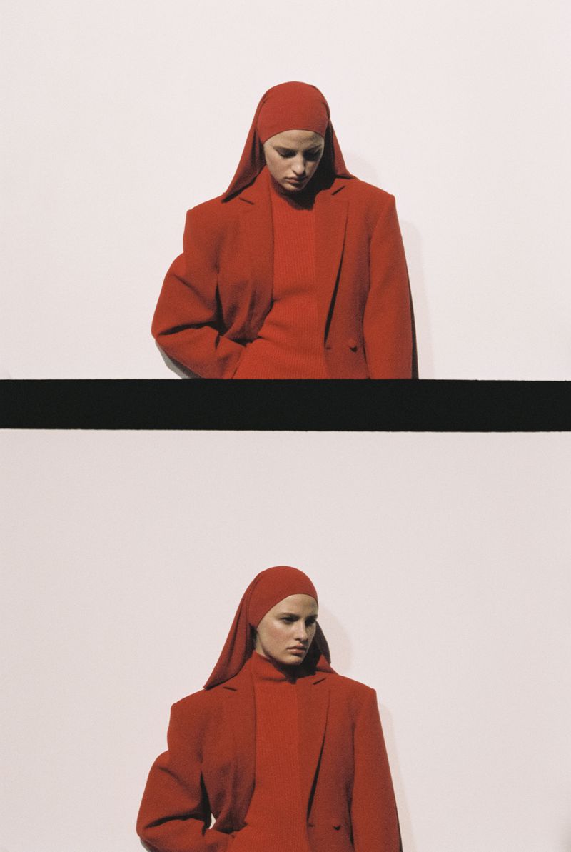 Elegant fashion shot of a woman in a red headscarf and suit, captured in a portrait with a graphic black stripe against a white backdrop.
