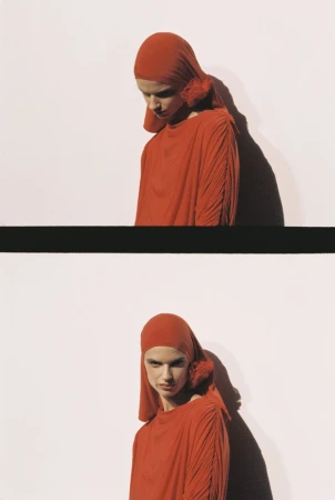 A woman wears a red hooded dress in a studio shot; shadows add depth to the composition against a white backdrop.