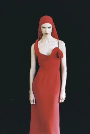 Model wearing a red dress and matching head covering against a black backdrop