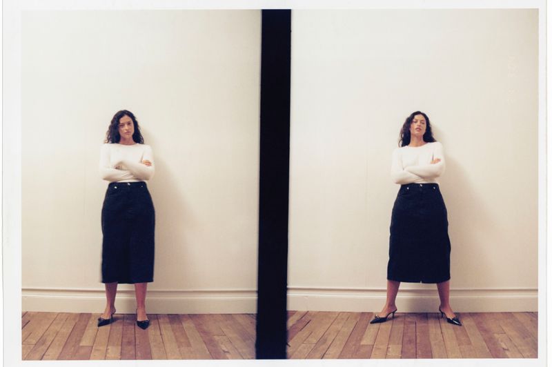 A young woman in a white sweater and black skirt stands in front of a white wall, duplicated side-by-side with a black vertical line in the middle.