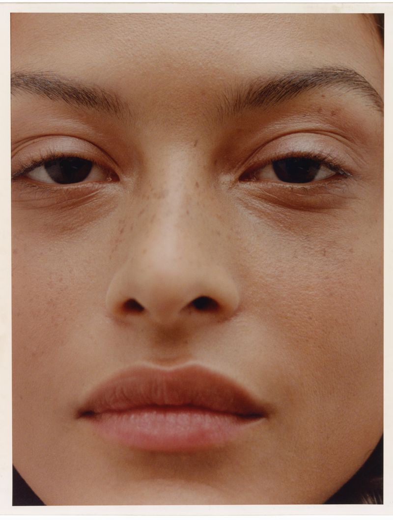 Close-up portrait of a woman with warm skin tones, dark eyes, and subtle freckles, emphasizing natural beauty and facial details.