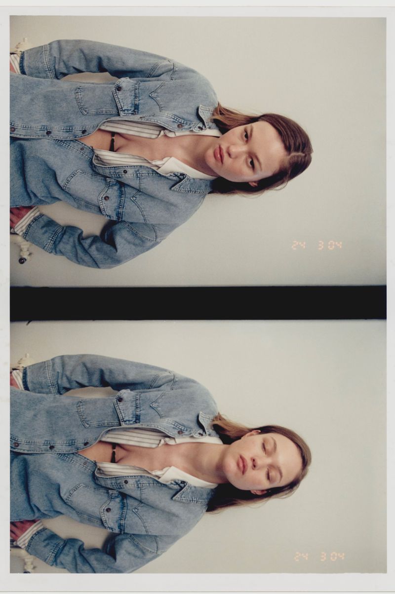 Woman with medium-length brown hair poses in a blue denim jacket and white shirt, captured with natural lighting in a close-up portrait.