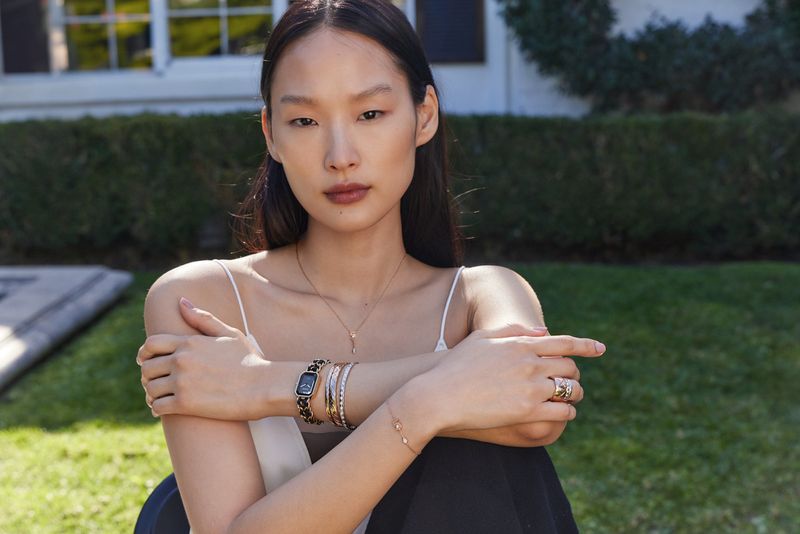 Model Yoonmi Sun wearing delicate jewellery outdoors against a garden background for Saks SP24 fashion campaign