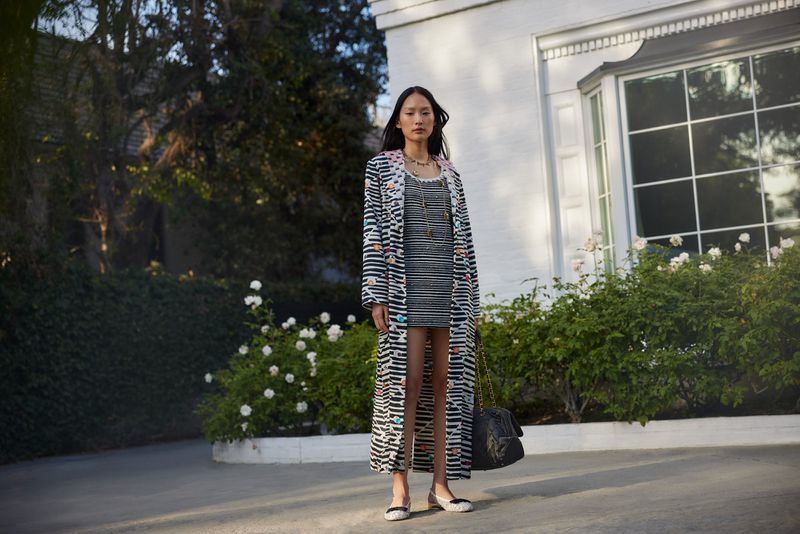 Model standing outdoors wearing a striped coat and dress in front of a white building exterior