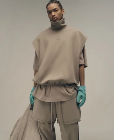 Male fashion model posing in neutral toned top, shorts and pants set with aqua gloves in a neutral background for a fashion editorial.