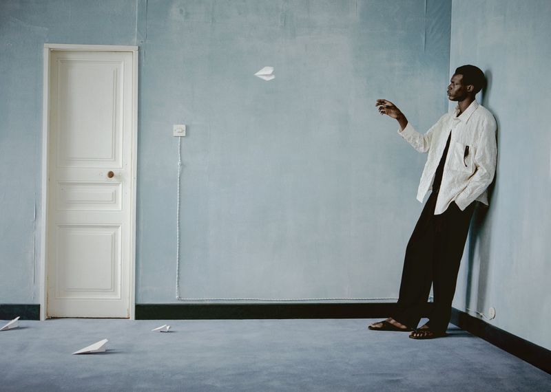 Man throwing paper airplane in blue room with light walls, dark trim, and gray carpet; creative lifestyle photography with indoor setting.