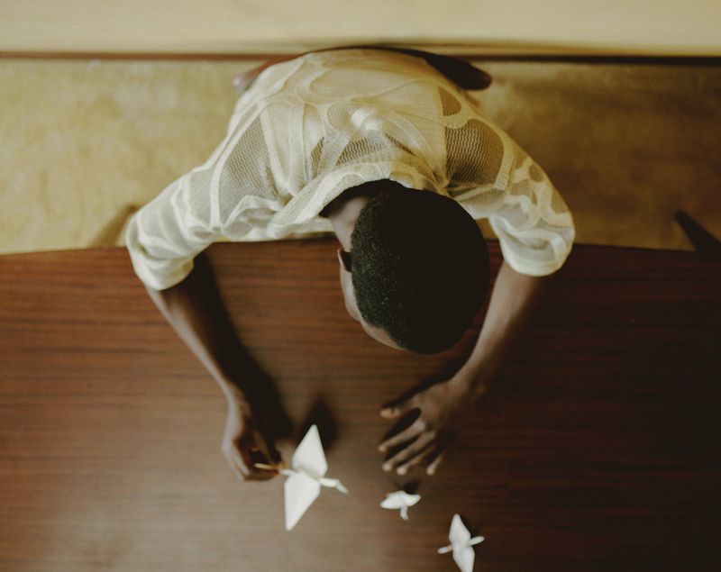 Overhead shot of an adult creating origami birds at a wooden table, illuminated by bright, soft lighting casting subtle shadows.