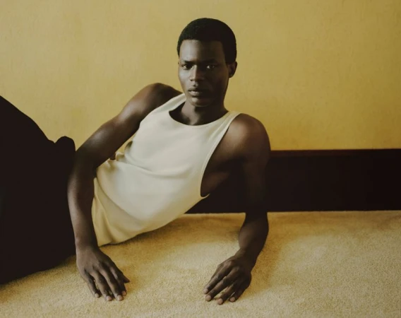 Model Mohammed Abubakar reclining on a beige carpeted floor wearing a cream tank top for Zara.