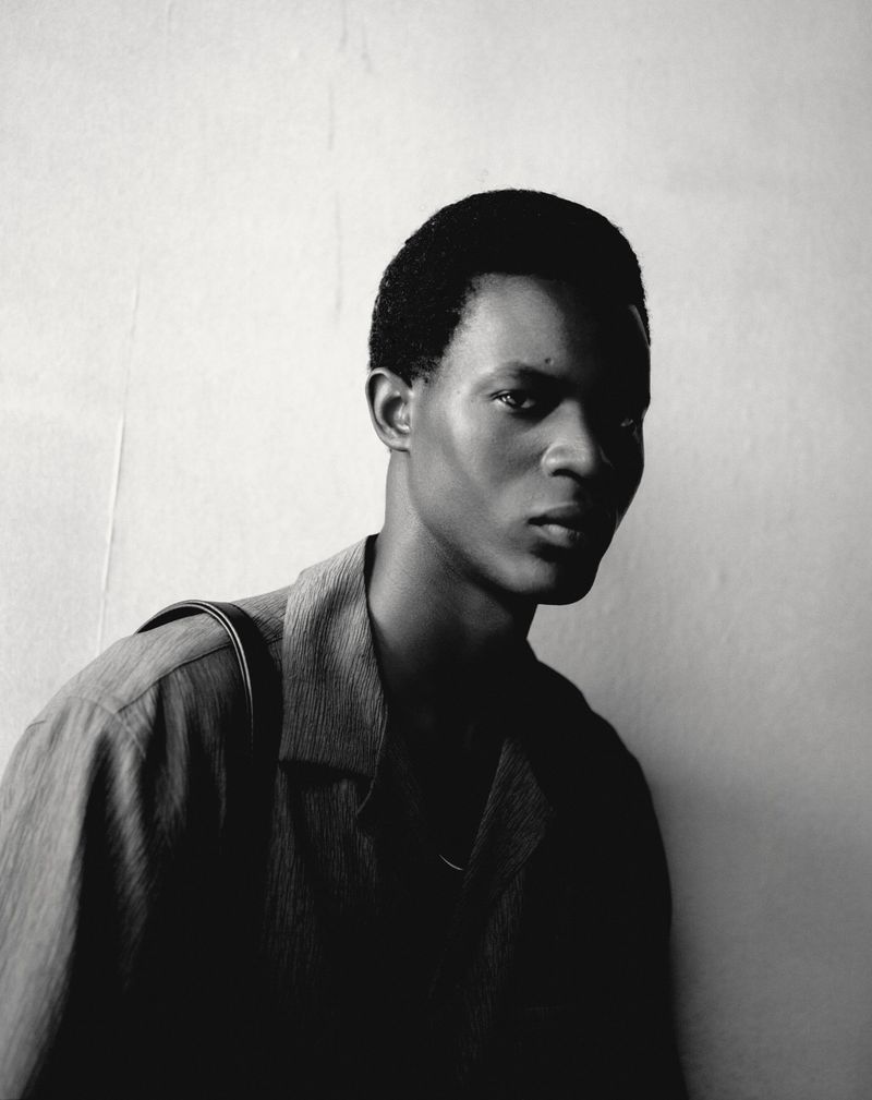 Monochromatic portrait of a Black male model wearing an open collared shirt with a shadow cast across the front of his body.