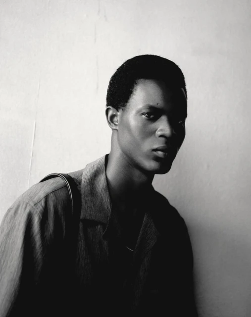 Monochromatic portrait of a Black male model wearing an open collared shirt with a shadow cast across the front of his body.