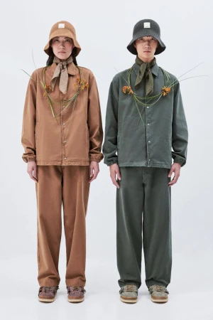 Two people stand side by side wearing matching casual outfits with bucket hats and flower details in a bright indoor photo studio setting.