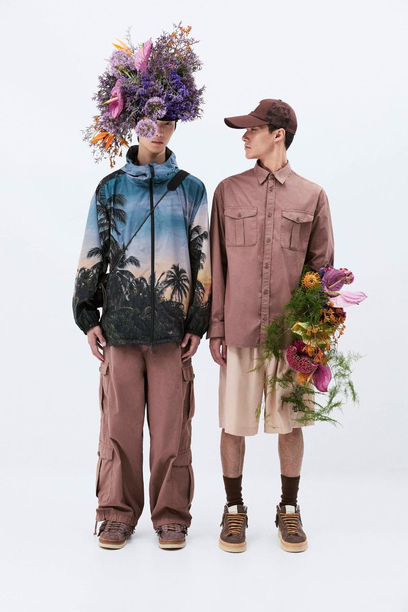 Two young adult models in casual fashion with unique floral headpieces and bouquets pose indoors against a white backdrop.