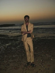 Model Ottawa Kwami standing on a rocky beach at dusk wearing a tan suit for Massimo Dutti