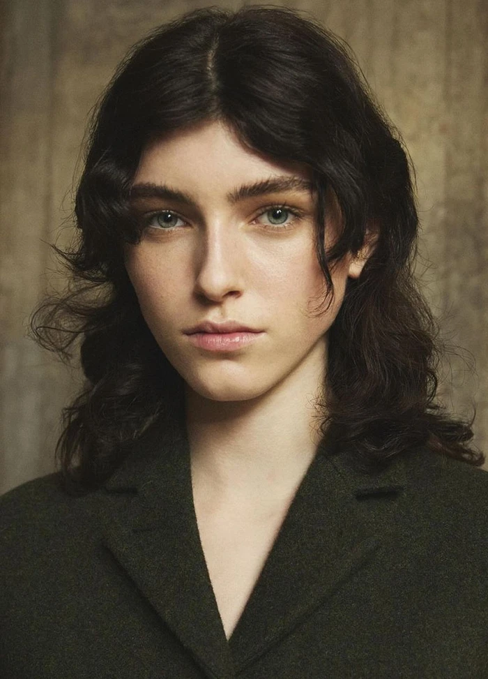 Portrait of a model with dark wavy hair and green jacket against a textured wall for Bally Fall Winter 2024