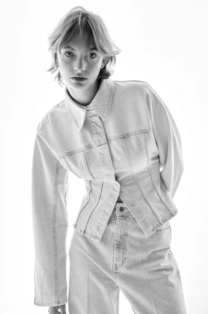 Model in light denim shirt and trousers posing against a bright white background for H&M Spring/Summer 2024 campaign.