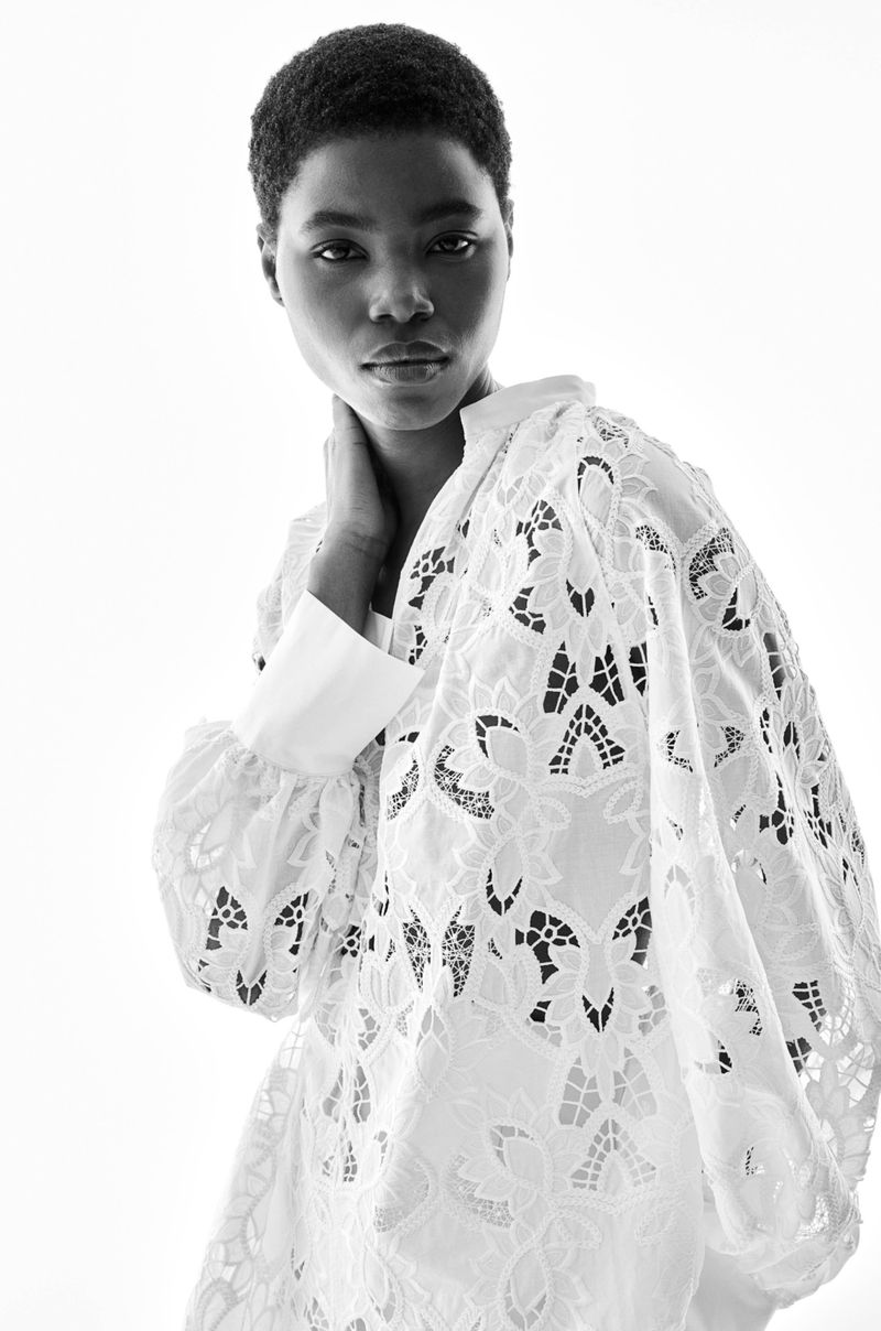 Black and white portrait of a Black woman wearing a white lace top, against a bright white backdrop, focusing on fashion and beauty.