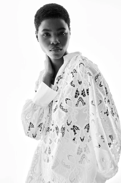 Black and white portrait of a Black woman wearing a white lace top, against a bright white backdrop, focusing on fashion and beauty.