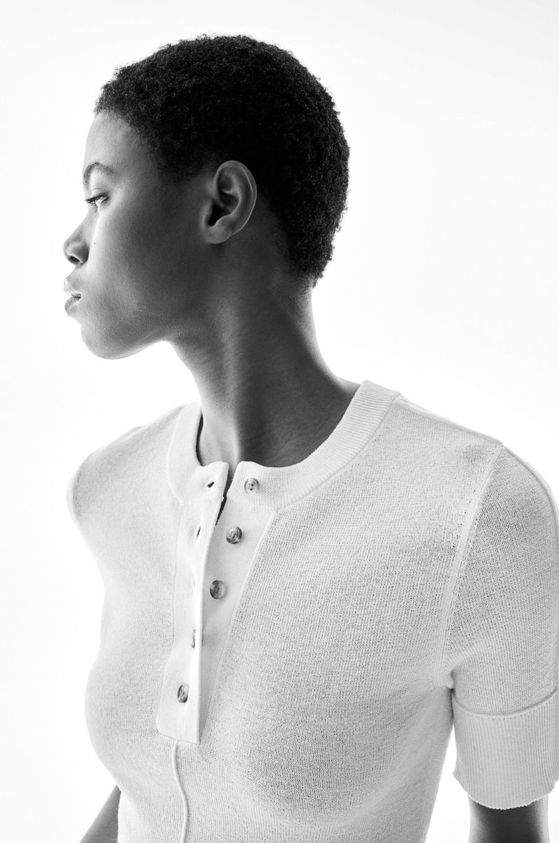 Portrait of a black female adult model in white textured button-down shirt looking left against a bright white background in black and white.