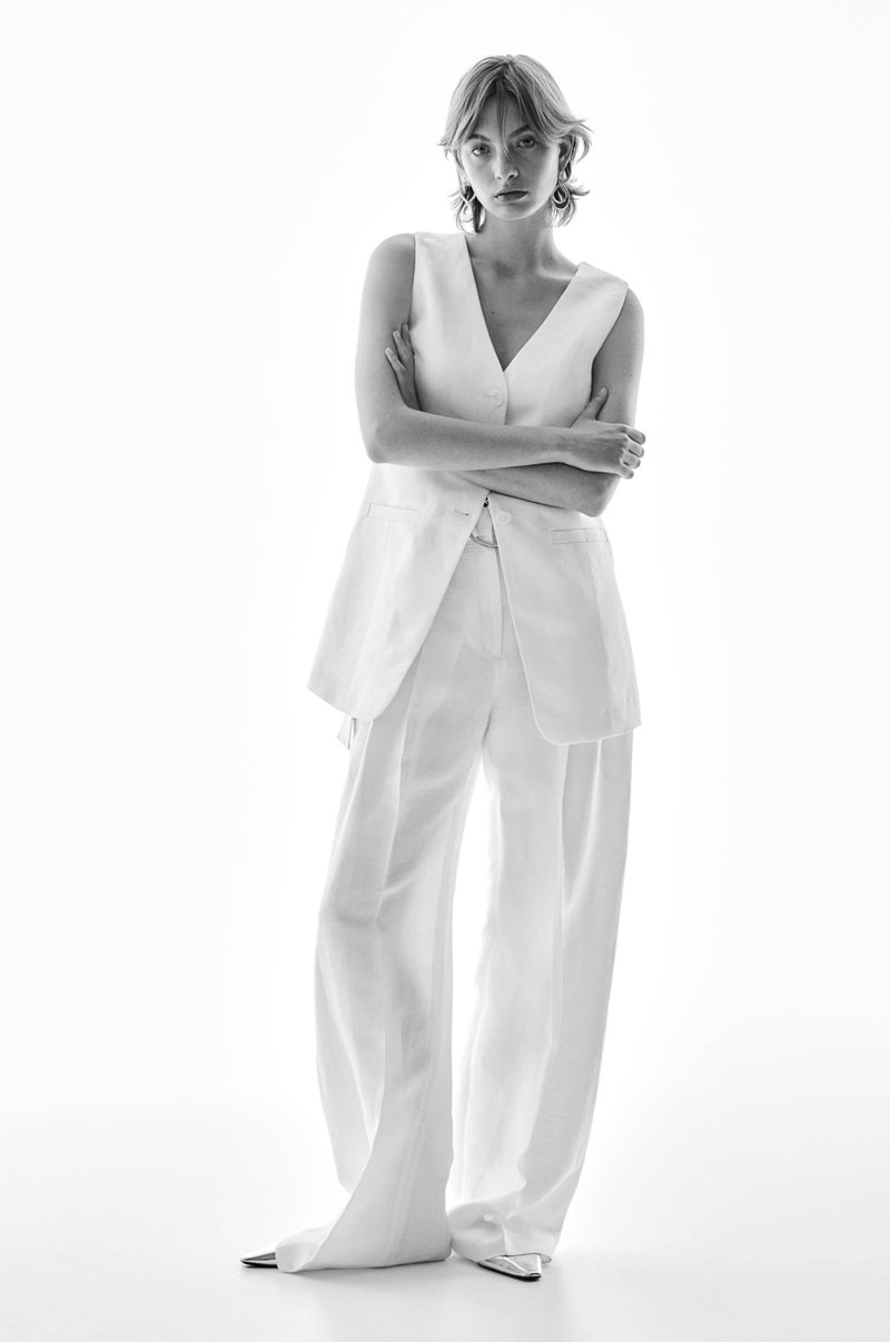 Black and white studio shot of a young adult woman posing in a white sleeveless top and matching wide-leg pants with arms crossed.