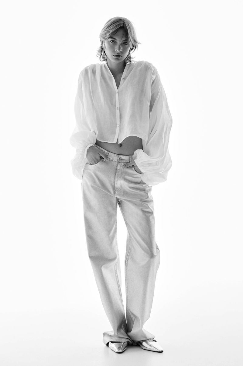 Monochrome fashion portrait of a woman wearing a white blouse and light jeans in a brightly lit studio.