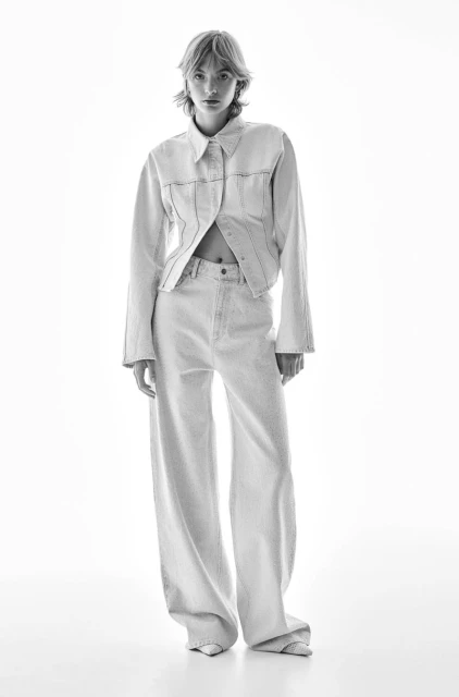 Monochrome full shot of a female model in a matching light-wash denim jacket and wide-leg jeans, set against a bright white backdrop.