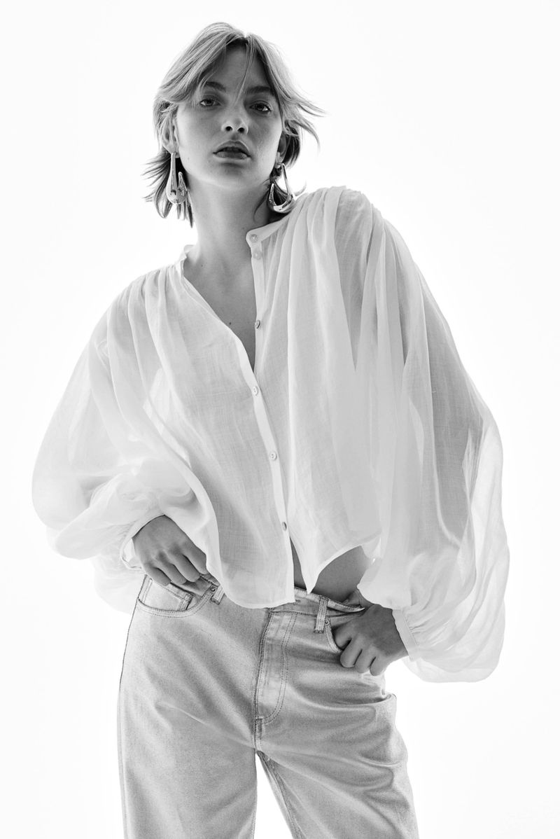 Model wearing a loose white button-up blouse and light wash jeans against a bright white background