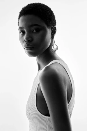 Model in white sleeveless ribbed top with silver drop earring against a bright white background