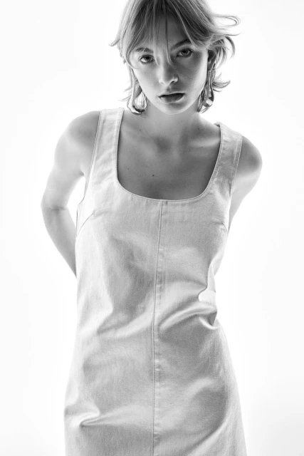 A young woman poses in a simple denim dress against a bright white backdrop, creating a clean, high-key fashion image.