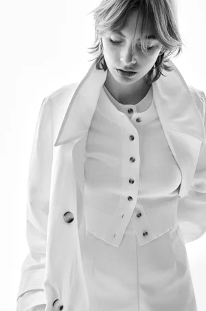 Model in white cardigan and jacket against a plain bright background