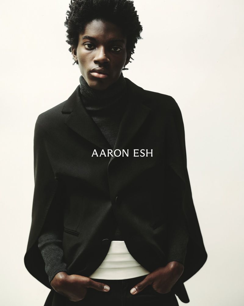 Portrait of an African American man in a black turtleneck, suit jacket, and dress pants posing against a neutral background.