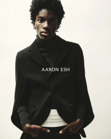 Portrait of an African American man in a black turtleneck, suit jacket, and dress pants posing against a neutral background.