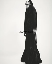 Monochrome fashion image of a model wearing a dark flowing gown looking upward against a plain white background with Aaron Esh text